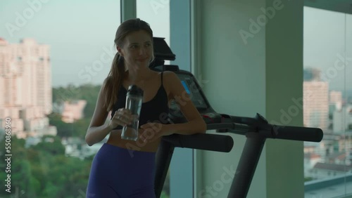 Young woman drinking water in the gym and smiling
