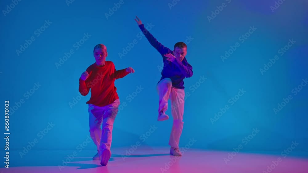 Stylish man and woman dancing contemp dance in bright sportive clothes on blue background at dance hall in neon light. Youth, music, style Stylish man and woman dancing contemp dance in bright sportive clothes on blue background at dance hall in neon light. Youth, music, style