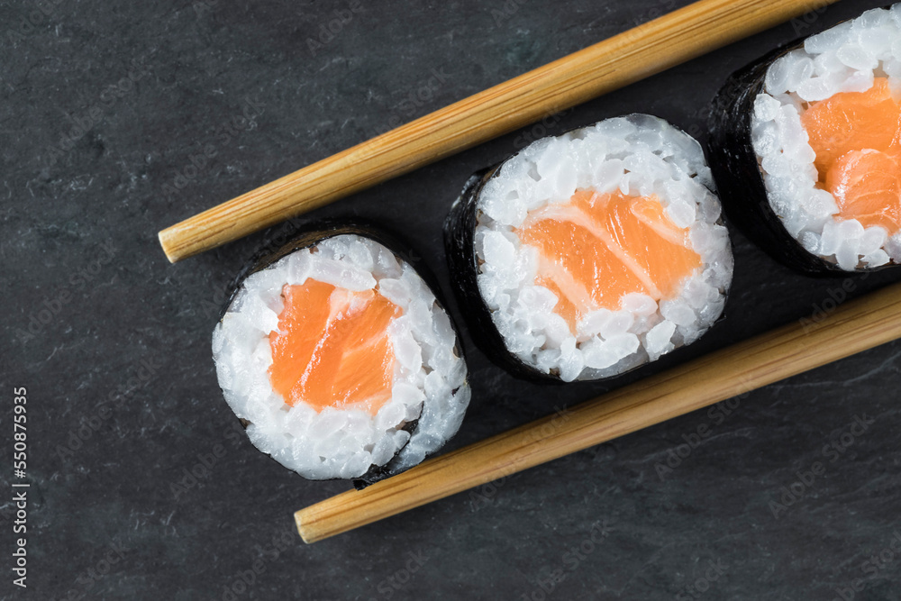 Macro top view of 3 salmon makis lined up on a black stone background with a toothpick on each side. Oriental, Japanese food. Takeaway. Macro top view of 3 salmon makis lined up on a black stone background with a toothpick on each side. Oriental, Japanese food. Takeaway.