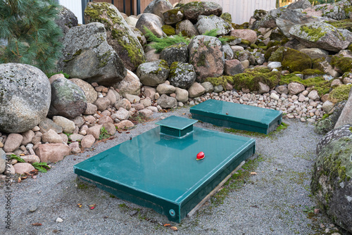 Square green metal cover of an autonomous septic tank with a warning lamp on the backyard among rocks. Sewer system of the house photo
