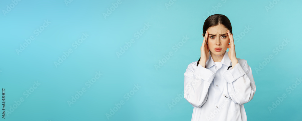 Image of woman doctor, medical personel grimacing from discomfort, having headache, migraine, feeling deezy, standing over torquoise background - obrazy, fototapety, plakaty 