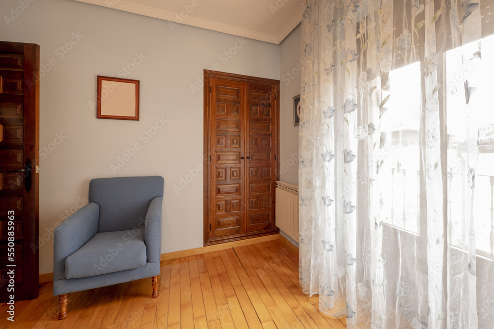 Fototapeta premium Corner of a bedroom with natural wood flooring, a built-in wardrobe with paneled doors and a blue fabric single armchair