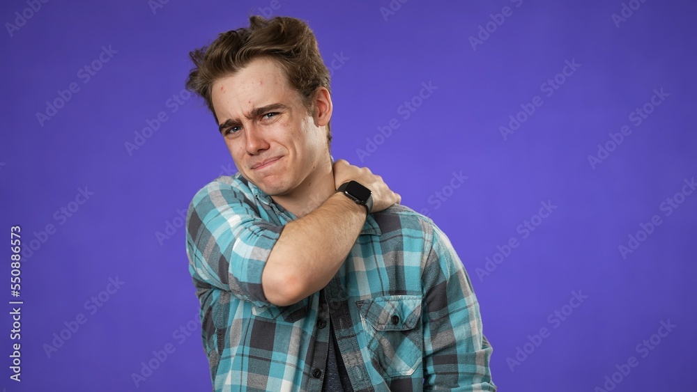 Naklejka premium Portrait of young hipster man 20s with sore neck shoulder problem isolated on purple background in studio