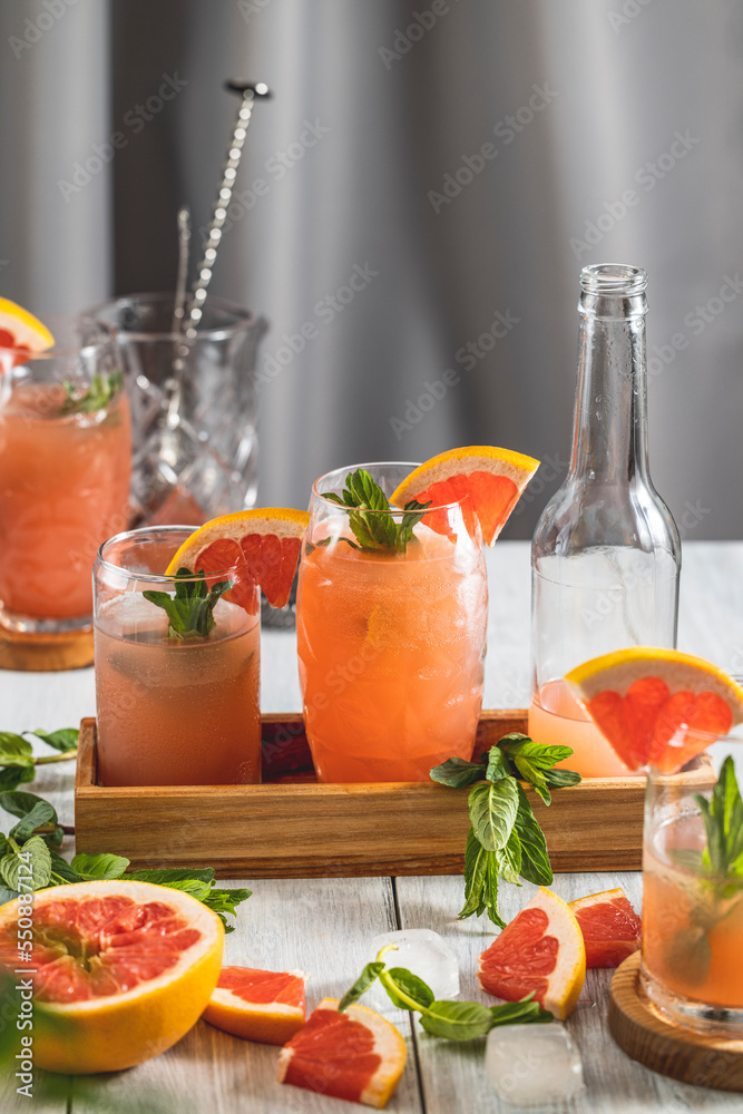 Grapefruit Cocktail in highball glasses or mocktails surrounded by ingredients and bar tools on light gray table surface Grapefruit Cocktail in highball glasses or mocktails surrounded by ingredients and bar tools on light gray table surface