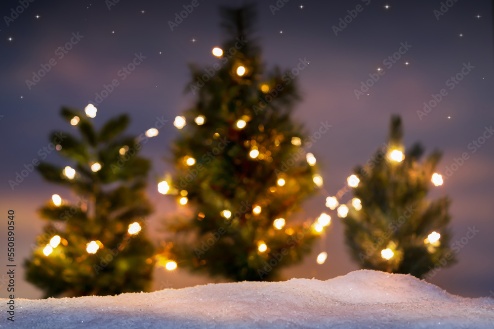 unfocused bright christmas trees in a row behind sharply snow cover, merry christmas or happy new year card concept with copy space
