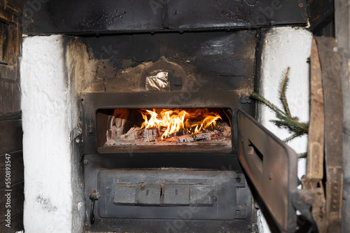 A bright fire burns in an old stove with an open metal door, copy space