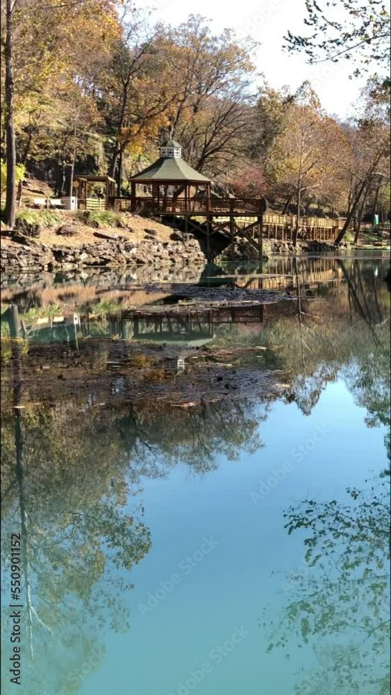 Panning scenic view of a natural spring with colorful trees reflected in the waters in autumn, vertical Panning scenic view of a natural spring with colorful trees reflected in the waters in autumn, vertical