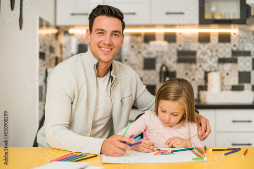 Little girl and her father enjoy drawing together at their home. 