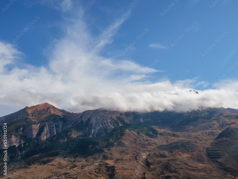 Mountain in the white clouds. Bright atmospheric scenery on top of mountain ridge above clouds in thick low clouds.  Beautiful mountain foggy scenery on abyss edge with sharp stones.