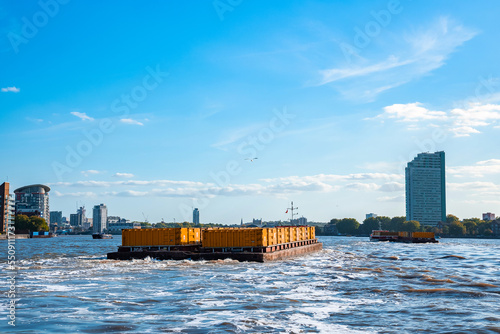 London, England. May 7, 2022. Industrial barge passing business center in London on the River Thames.
