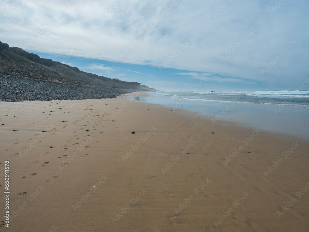View of empty Praia do Queimado beach with ocean waves and sharp rocks and wet golden sand at wild Rota Vicentina coast near Porto Covo, Portugal. View of empty Praia do Queimado beach with ocean waves and sharp rocks and wet golden sand at wild Rota Vicentina coast near Porto Covo, Portugal.