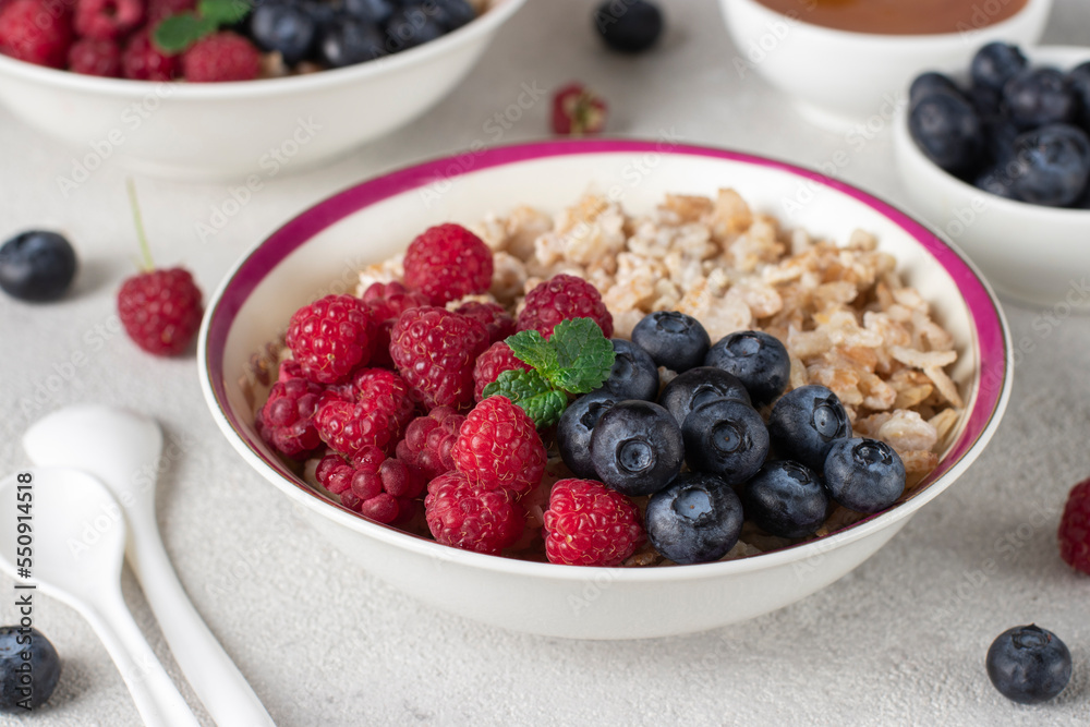 Oatmeal porridge with blueberries, raspberry and honey on light gray background. Breakfast meal concept, Close-up Oatmeal porridge with blueberries, raspberry and honey on light gray background. Breakfast meal concept, Close-up