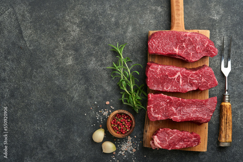 Raw steaks. Top blade steaks on wood burning board with spices, rosemary, vegetables and ingredients for cooking on black background. Top view.  Copy space.