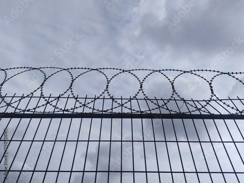 barbed wire fence. An iron fence with barbed wire on top against a cloudy gray sky