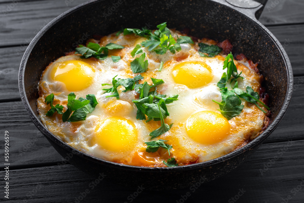 Shakshuka eggs in a skillet against a black wooden backdrop. Poached