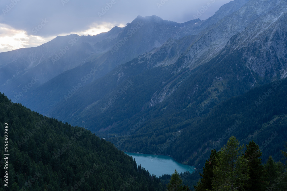 Landscape of Hochgall mountain peaks covered by clouds, valley and Antholzer See lake in Dolomites, Italy