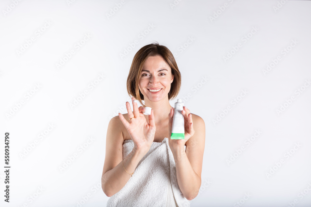 Young and beautiful woman stands after bathing, smiles and demonstrates her cream for face isolated on white background Young and beautiful woman stands after bathing, smiles and demonstrates her cream for face isolated on white background
