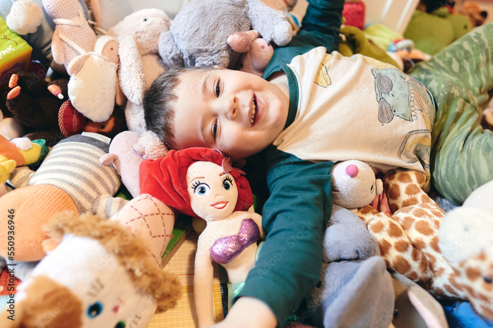 happy young boy playing among a mountain of soft plush toys