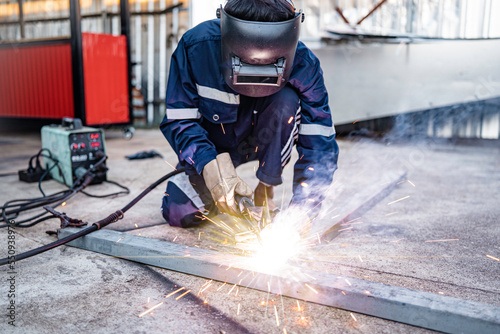 Welding, male worker welding metal workpiece outside factory, protective clothing protective gloves and safety helmet, welding sparks and light photo