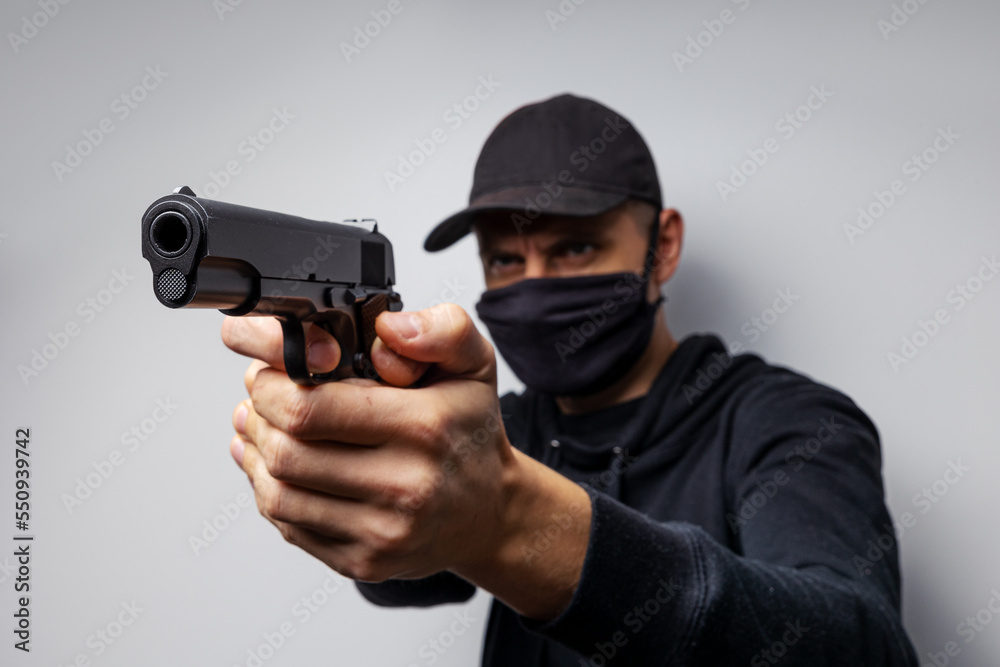 Unrecognisable male person in the black mask and pistol, outlaw and crime concept Unrecognisable male person in the black mask and pistol, outlaw and crime concept