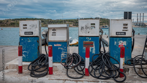 Four older type fuel pumps in a marina used for ships, with a lot of hose around. Refinery in the background. photo
