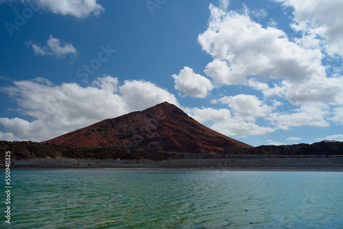 Red colored mountain landscape with lake and blue sky with clouds