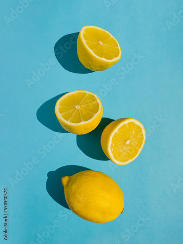 Juicy whole and half lemon and slices on bright pastel blue background. Minimal top view summer concept.