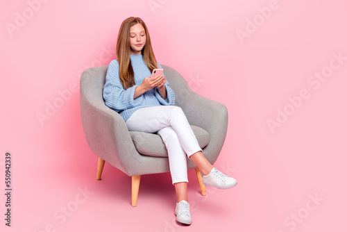 Full body size photo of young teen age schoolgirl brown hair wear blue knitted pullover chatting online sit sofa isolated on pink color background