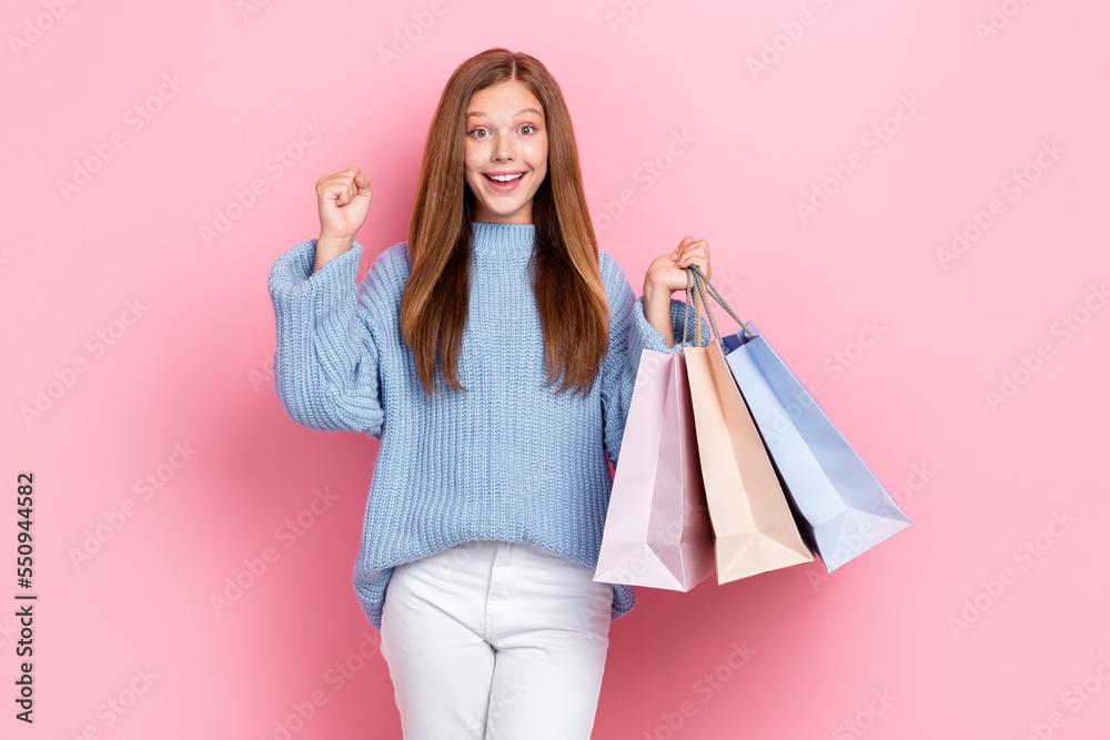 Photo poster of funny cute schoolgirl beautiful impressed positive teenager hold stack bags fists up hooray isolated on pastel pink color background