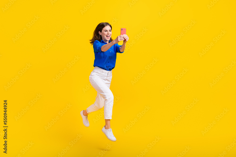 Full length photo of excited pretty lady wear blue shirt jumping high recording video vlog device isolated yellow color background