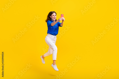 Full length photo of excited pretty lady wear blue shirt jumping high recording video vlog device isolated yellow color background © deagreez