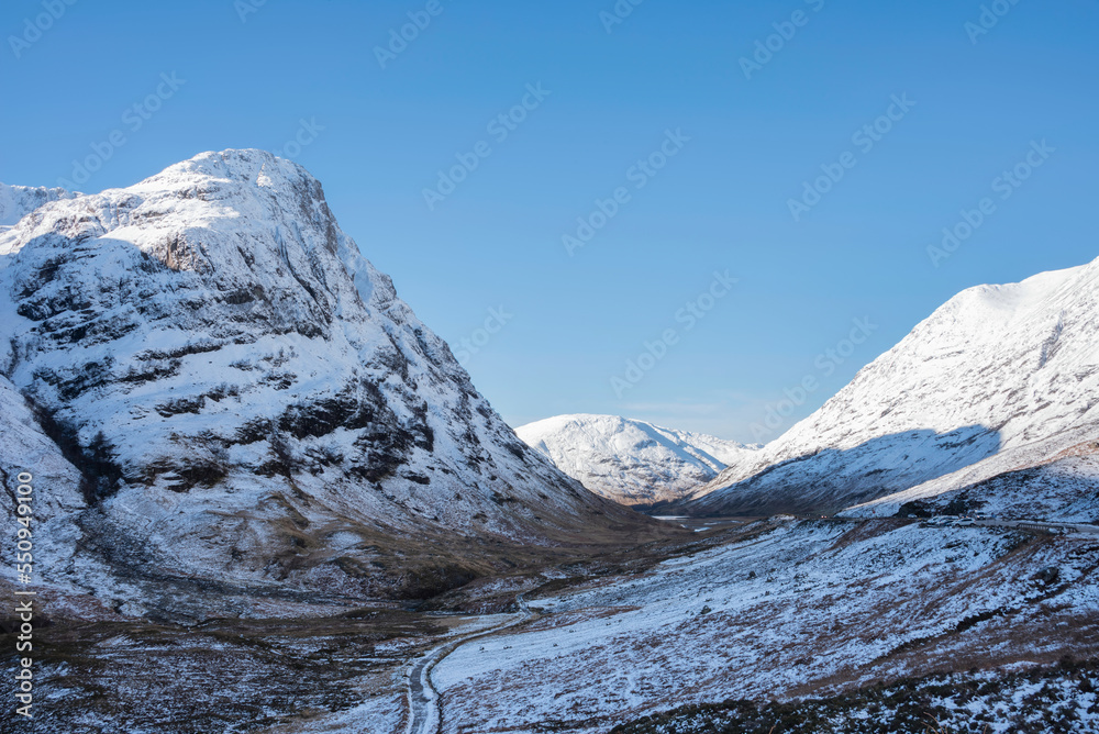 Gorgeous Winter landscape blue sky image of view along Glencoe Rannoch Moor valley with snow covered mountains all around