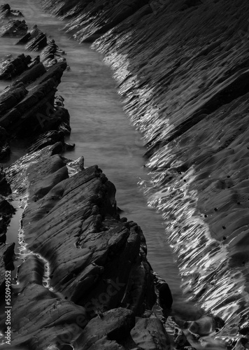 Abstract landscape picture of rocks on Welcome Mouth Beach at sunset with tide marks on rocks reflecting sunlight