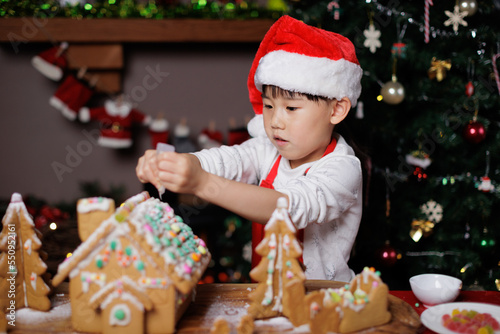 young girl wearing Santa hat was decorating gingerbread house for celebrating Christmas at home