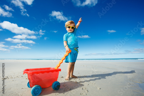 Cute blond boy in sunglasses play on ocean beach smile lift hand