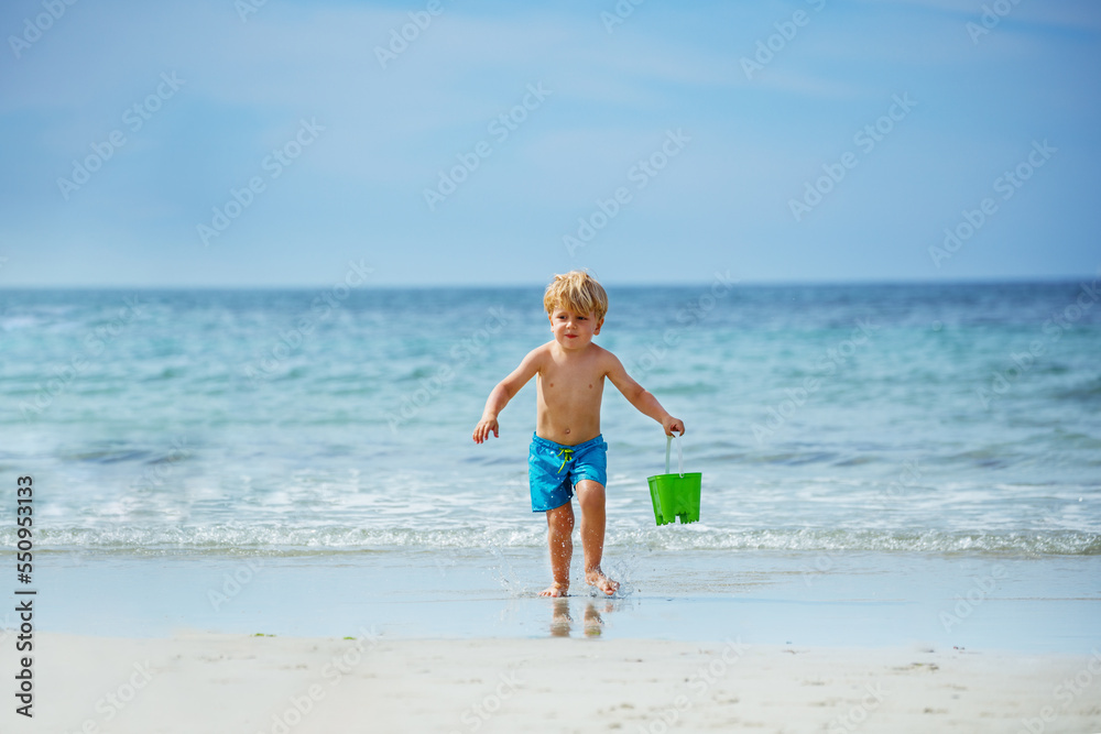 Cute little blond boy run with bucket on ocean beach from waves Cute little blond boy run with bucket on ocean beach from waves