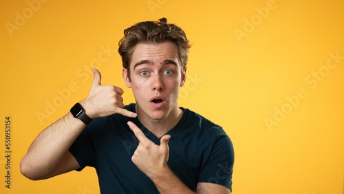 Fotografía Portrait of smiling happy young man 20s smiling and giving call me gesture with hands isolated on yellow background