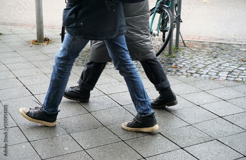 Schuhe und Beine von Mutter und jugendlichem Sohn beim Laufen über grauem Steinplattenplatz in Stadt am Nachmittag im Winter