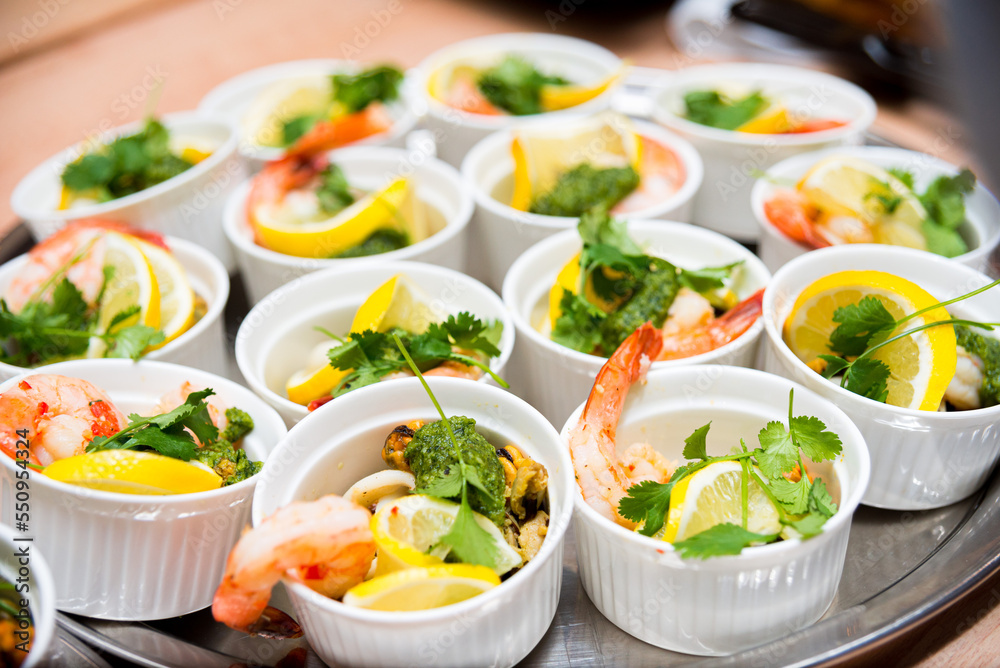 Many servings of seafood with lemon in ramekins, shrimp, mussels and squid rings garnished with cilantro leaves Many servings of seafood with lemon in ramekins, shrimp, mussels and squid rings garnished with cilantro leaves