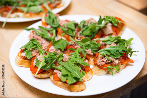 A plate of tuna tapas with stewed red bell peppers and arugula leaves