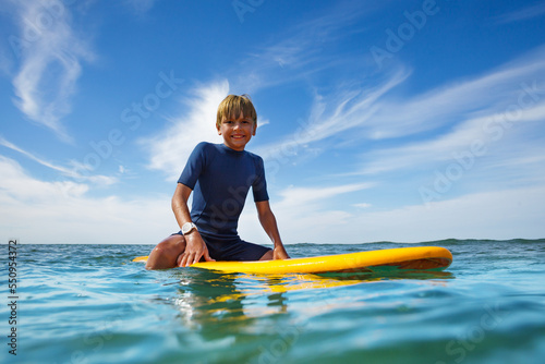 Cute young boy sit on orange surfboard in ocean