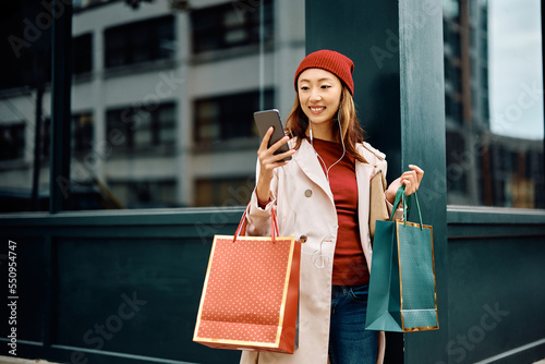 Happy Asian woman text messaging on cell phone while shopping in city. photo