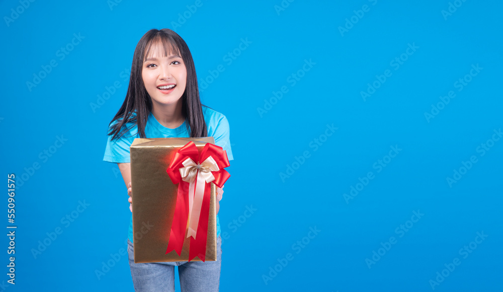 Cheerful asian woman holding gift box giving surprise family in festive eve season celebration or anniversary standing on blue background. Cute young girl give celebrate gift box gold over isolated. Cheerful asian woman holding gift box giving surprise family in festive eve season celebration or anniversary standing on blue background. Cute young girl give celebrate gift box gold over isolated.