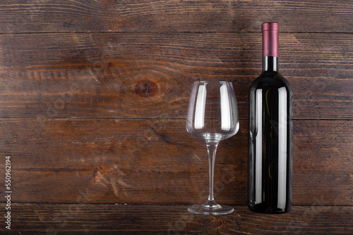 Bottle of red wine and an empty glass on a wooden background.