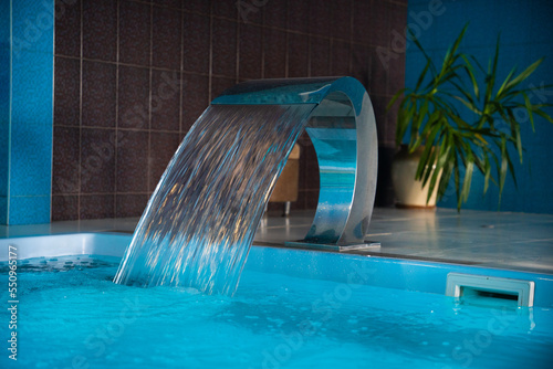 a modern large indoor pool with blue lighting and a waterfall.