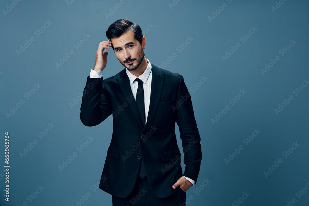 A business man looks thoughtfully into the camera in a black suit, white shirt, brunette with a beard on a blue background A business man looks thoughtfully into the camera in a black suit, white shirt, brunette with a beard on a blue background