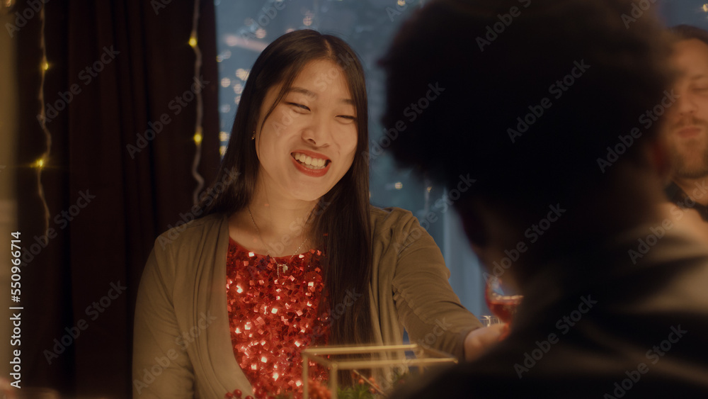 Asian woman drinks wine, talks and smile. Multi cultural friends celebrating Christmas or New Year 2023. Served holiday table. Warm atmosphere of Christmas dinner at home. Christmas party. Asian woman drinks wine, talks and smile. Multi cultural friends celebrating Christmas or New Year 2023. Served holiday table. Warm atmosphere of Christmas dinner at home. Christmas party.