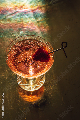 pink sparkling wine drink in cut crystal champagne coupe with strawberry heart garnish on cocktail pick sitting on brass table