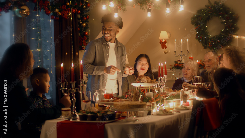 African American man cuts turkey with knife. Multi cultural family celebrating Christmas or New Year. Served holiday table with dishes and candles. Warm atmosphere of family Christmas dinner at home. African American man cuts turkey with knife. Multi cultural family celebrating Christmas or New Year. Served holiday table with dishes and candles. Warm atmosphere of family Christmas dinner at home.