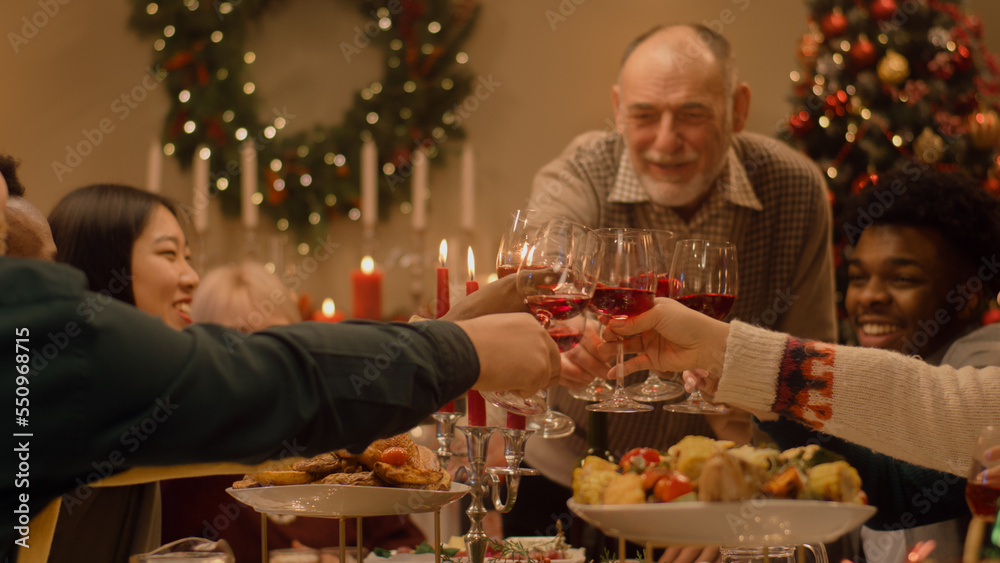Happy multi cultural family celebrating Christmas or New Year, raising wineglasses. Served holiday table with different dishes and candles. Warm atmosphere of family Christmas dinner at home. Cheers. Happy multi cultural family celebrating Christmas or New Year, raising wineglasses. Served holiday table with different dishes and candles. Warm atmosphere of family Christmas dinner at home. Cheers.